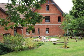 A brick building with a sloped roof, a grassy yard with a play area, and a swing set. - Holiday apartment with 2 bedrooms (Walsrode)