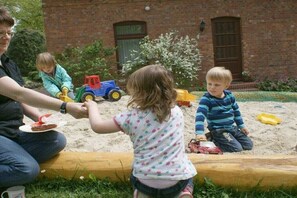 A family with children playing in a sandbox in front of a brick building. - Holiday apartment with 2 bedrooms (Walsrode)
