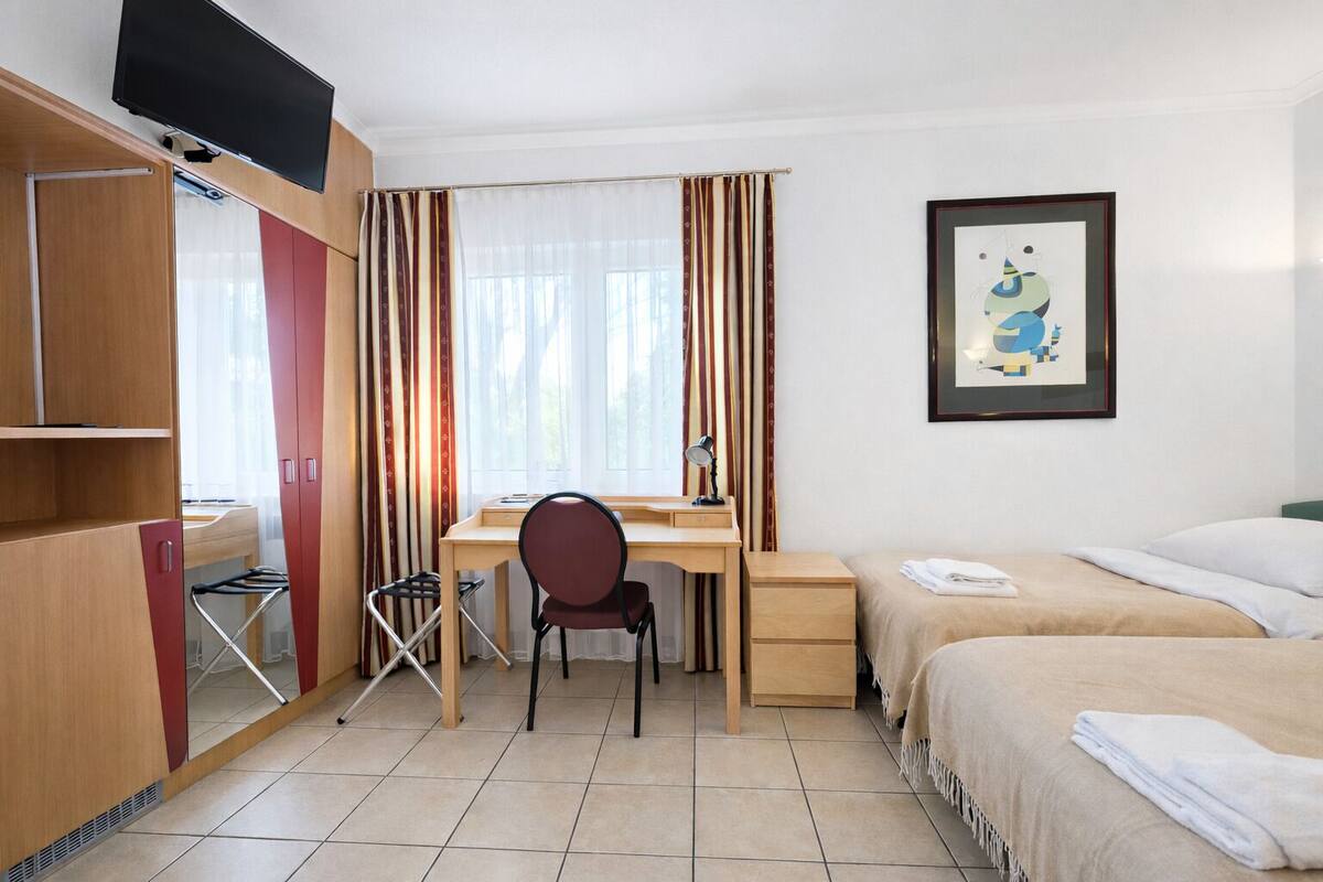 A hotel room with a bed, desk, chair, TV, and curtains.