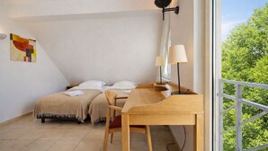 Une chambre avec deux lits, un bureau, une chaise, une lampe et une fenêtre donnant sur des arbres.