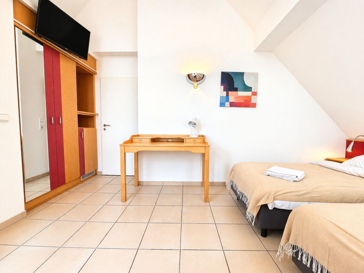 Una camera da letto con un letto, una scrivania, un armadio, una TV e una lampada a muro.