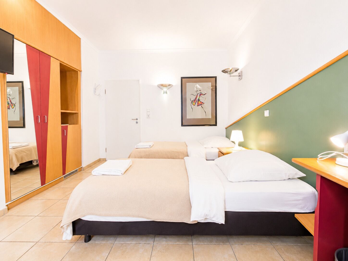 Quarto de hotel com cama, escrivaninha, cadeira, guarda-roupa e uma obra de arte emoldurada na parede.
