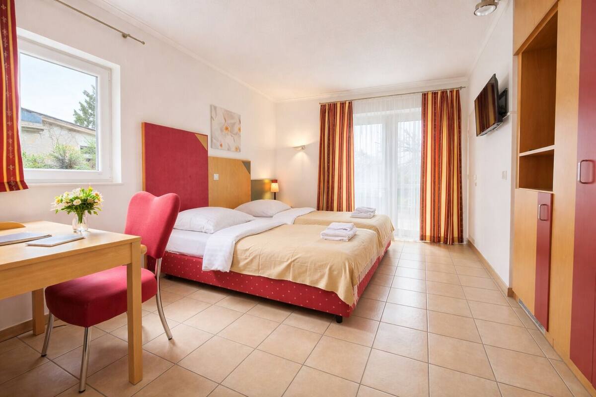 A hotel room with a bed, a desk, a chair, a TV, and a window with curtains.