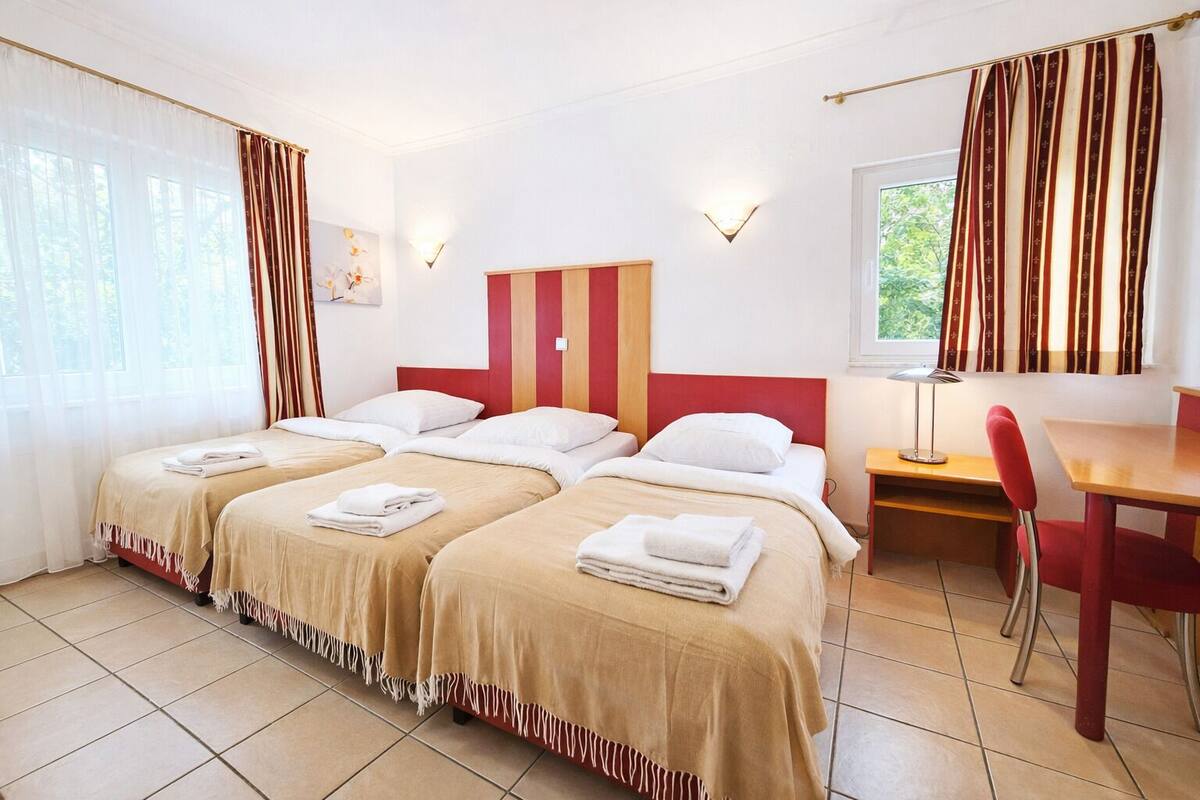 A hotel room with two beds, a desk, a chair, and a window with curtains.