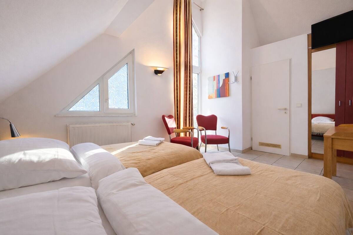 A bedroom with a sloped ceiling, a large bed, two chairs, a table, and a painting on the wall.