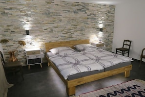 Ein Schlafzimmer mit einem hölzernen Bett, Nachttischen, einem Sessel und einer Wand mit Struktur.