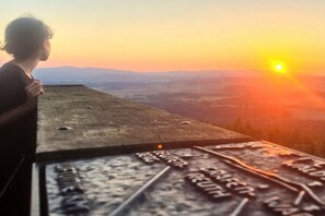 Eine Person blickt auf eine Landschaft mit Sonnenuntergang.