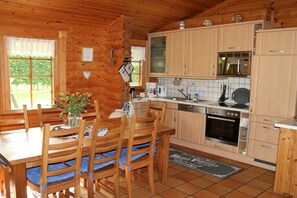 Ein Holzblockhaus-Interieur mit Esstisch, Stühlen, einer Küche mit Herd, Backofen und Schränken.