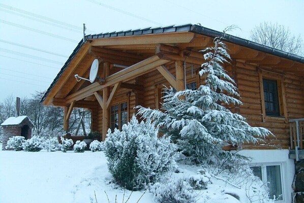 Eine Holzhütte mit geneigtem Dach, einer Satellitenschüssel und schneebedeckter Vegetation.