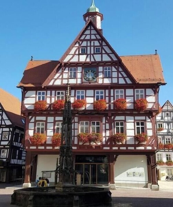 Ein traditionelles Fachwerkhäuschen mit einer Uhr, Fenstern und Blumenkästen.