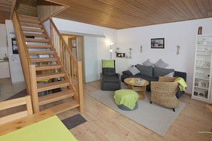 Ein Wohnzimmer mit einer Holztreppe, einem grauen Sofa, einem Korbstuhl und einem kleinen runden Tisch.