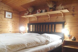 Una camera in una baita di legno con un letto, mensole con oggetti decorativi e un quadro appeso al muro.