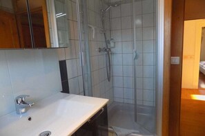 Un baño con lavamanos blanco, espejo y zona de ducha.