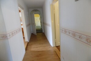 Ein schmaler Korridor mit Holzdielen und weißen Wänden, der zu einer Tür am Ende führt.