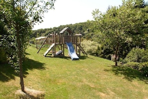 A wooden play structure with a slide in a grassy area surrounded by trees. - Holiday apartment with 2 bedrooms (Rickenbach)