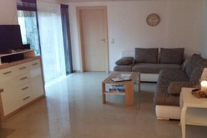 A living room with a sofa, a coffee table, a TV on a stand, and a door leading to another room. - Holiday apartment with 2 bedrooms (Rickenbach)