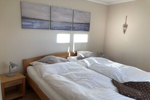 Ein Doppelbett mit weißer Bettwäsche, ein Nachttisch mit Lampe und eine herzförmige Wanddekoration.