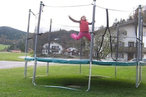 Ein Trampolin in einer grünen Wiese, im Hintergrund Häuser.