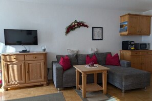 Ein Wohnzimmer mit grauem Sofa, einem Holztisch, einem Flachbildfernseher, einem Holzschrank und einem gerahmten Bild an der Wand.
