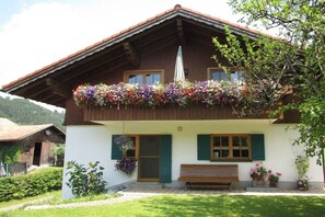 A traditional chalet with a balcony adorned with flowers, a wooden bench, and a small garden area. - Holiday apartment with 2 bedrooms (Oberstaufen)