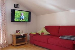 Ein rotes Sofa, ein an der Wand befestigtes Fernsehgerät, eine Holzunterhaltungsecke und ein gemustertes Vorhang.