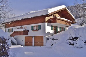 Eine zweistöckige Chalet mit Holzfassade, grünen Fensterläden und einem mit Schnee bedeckten Dach.