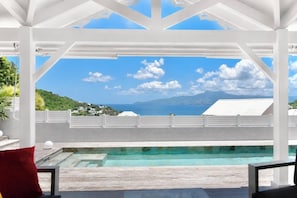 Ein Pool mit Blick auf das Meer und die Berge, weiße Säulen und ein rotes Kissen.