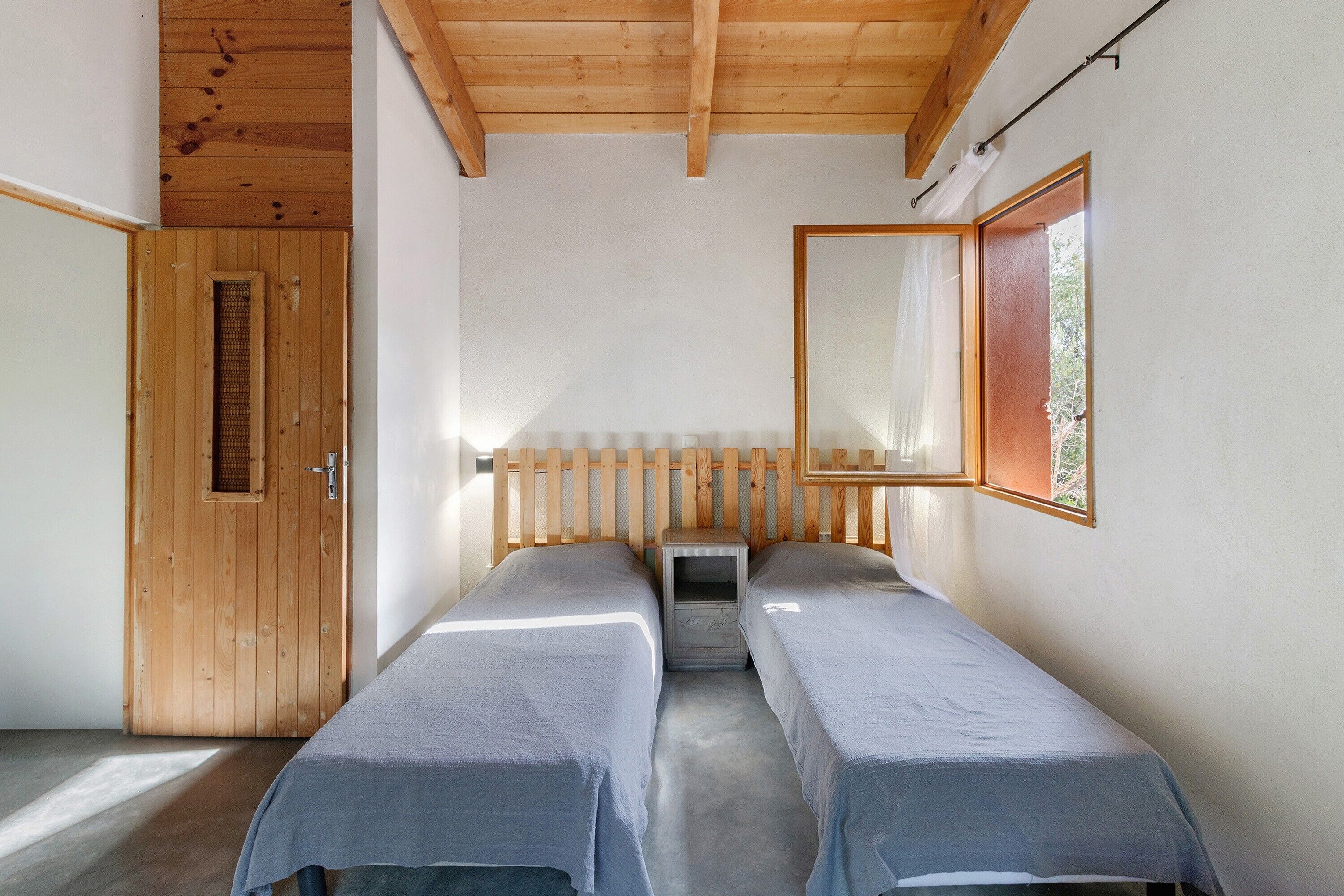 A room with two beds, a wooden door, a small table, and a window with a view.