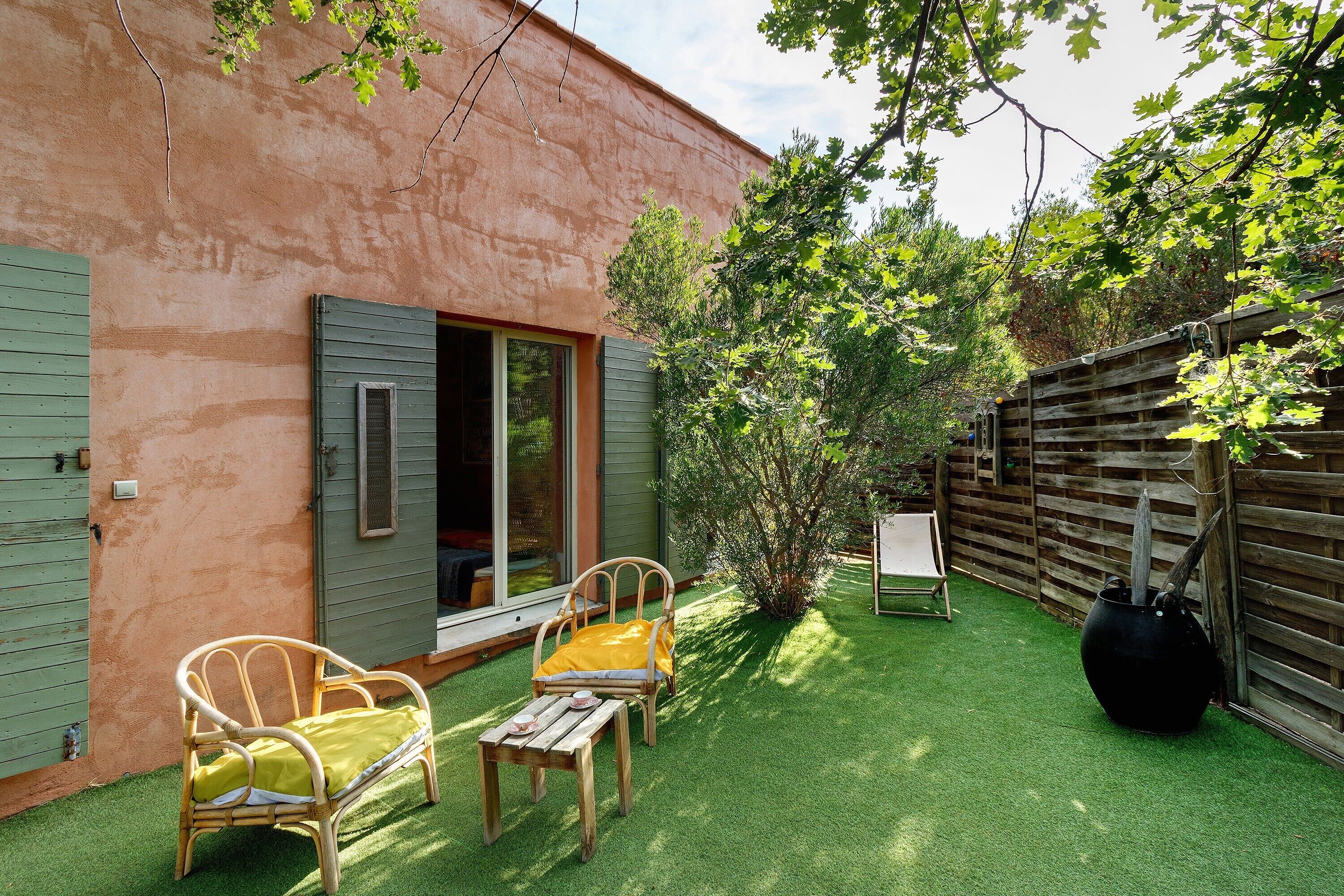 Un patio con una silla y una mesa, cerca de una valla de madera y un edificio con una puerta verde.