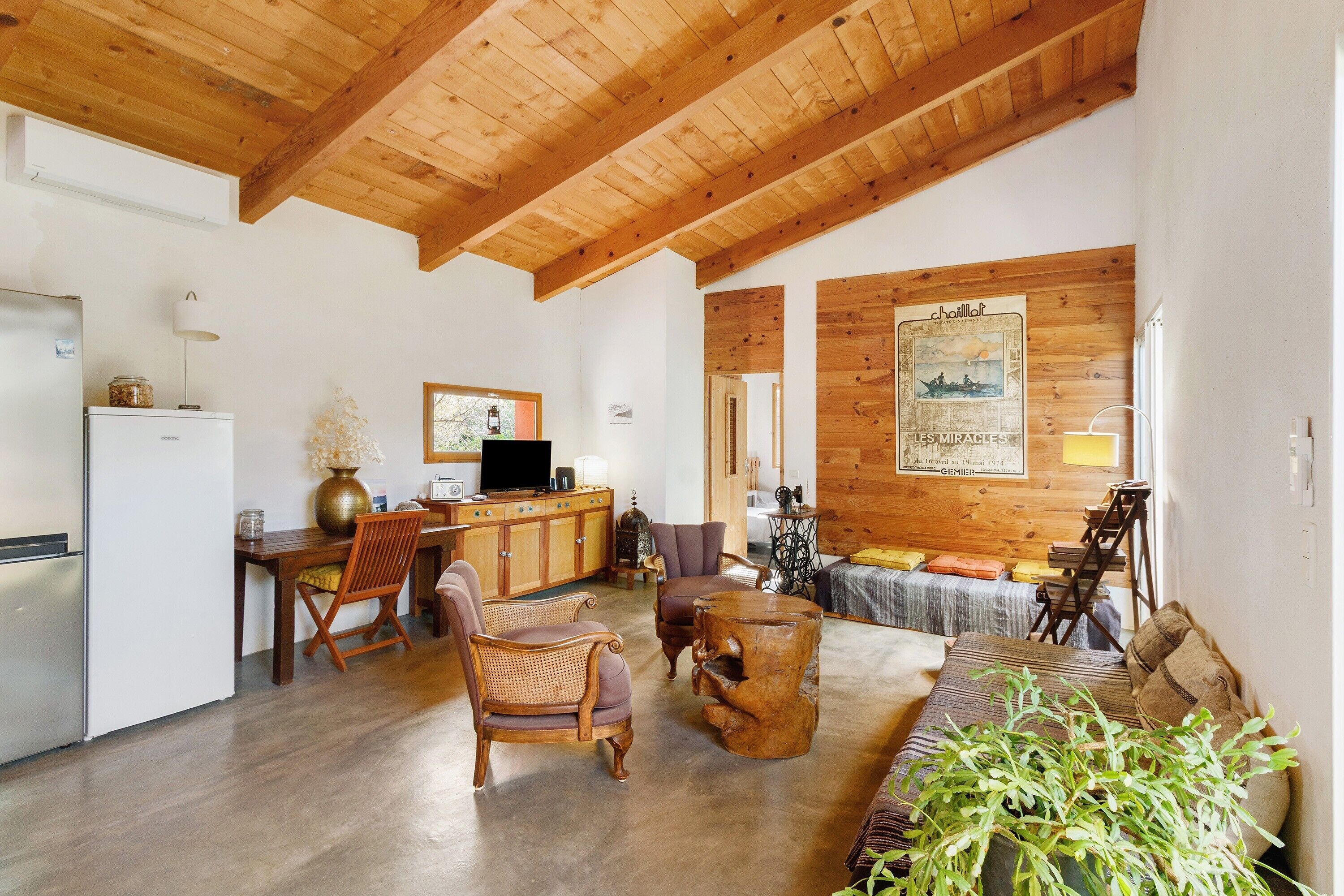 Un'ampia zona giorno con travi in legno, un tavolo da pranzo, sedie, un divano e un angolo cottura con frigorifero e computer.