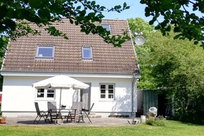 Een huis met twee verdiepingen, een betegeld dak, een terras met een tafel en stoelen, en een schotelantenne.