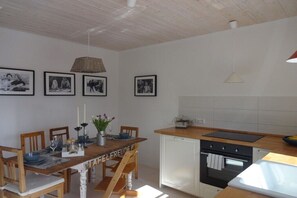Un coin repas avec une table et des chaises en bois, une cuisine équipée d’une cuisinière et d’un four, et des photographies en noir et blanc encadrées accrochées au mur.