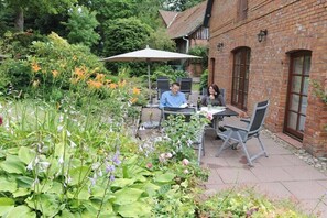 A brick building with a patio area featuring outdoor seating and a garden with various plants and flowers. - Holiday apartment with 2 bedrooms (Walsrode)