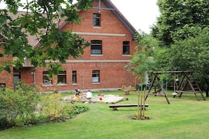 A two-story brick building with a garden area in front, including a swing set and play equipment. - Holiday apartment with 2 bedrooms (Walsrode)