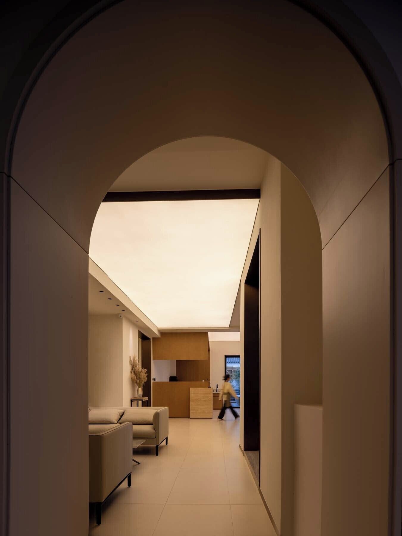 Un interior moderno con un pasillo que conduce a una sala de estar, que incluye un sofá, una zona de cocina y un amplio ventanal.