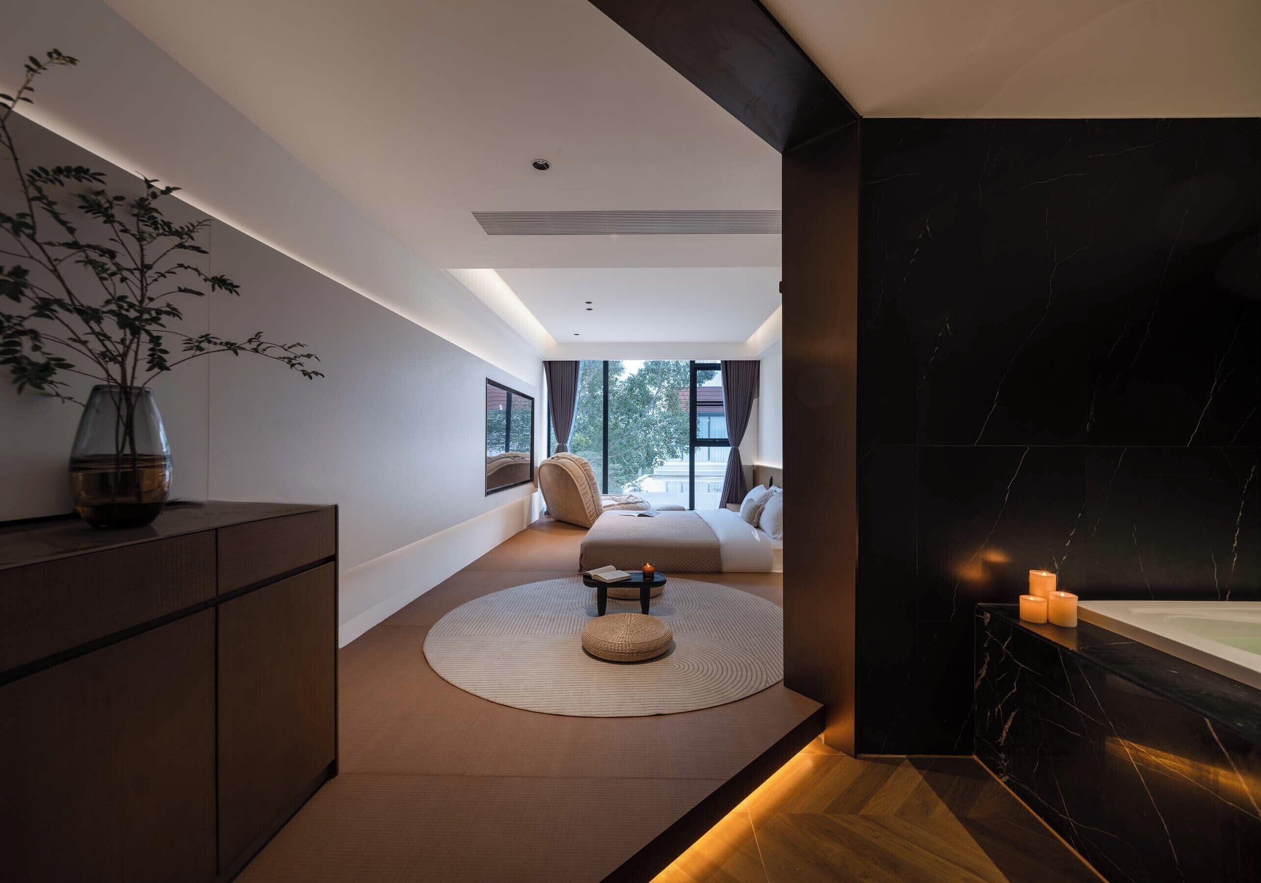 A modern bedroom with a large window, a round rug, a bedside table, and a nightstand.