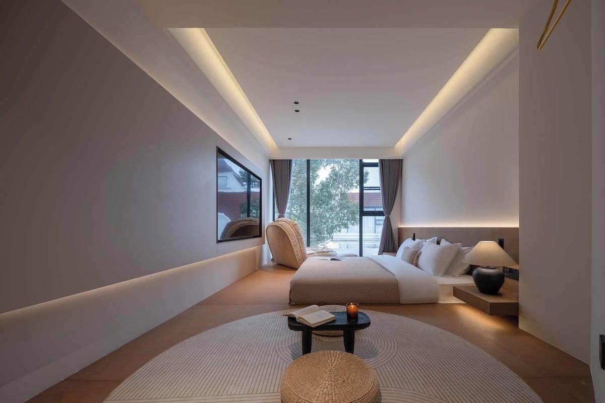 A modern hotel room with a large bed, a seating area, a small table, and a view of the outdoors.
