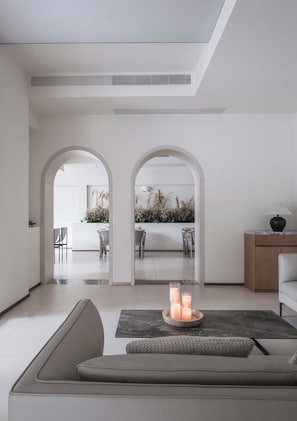 Un interior moderno con un sofá, una mesa con velas y una vista a través de un arco hacia un comedor.