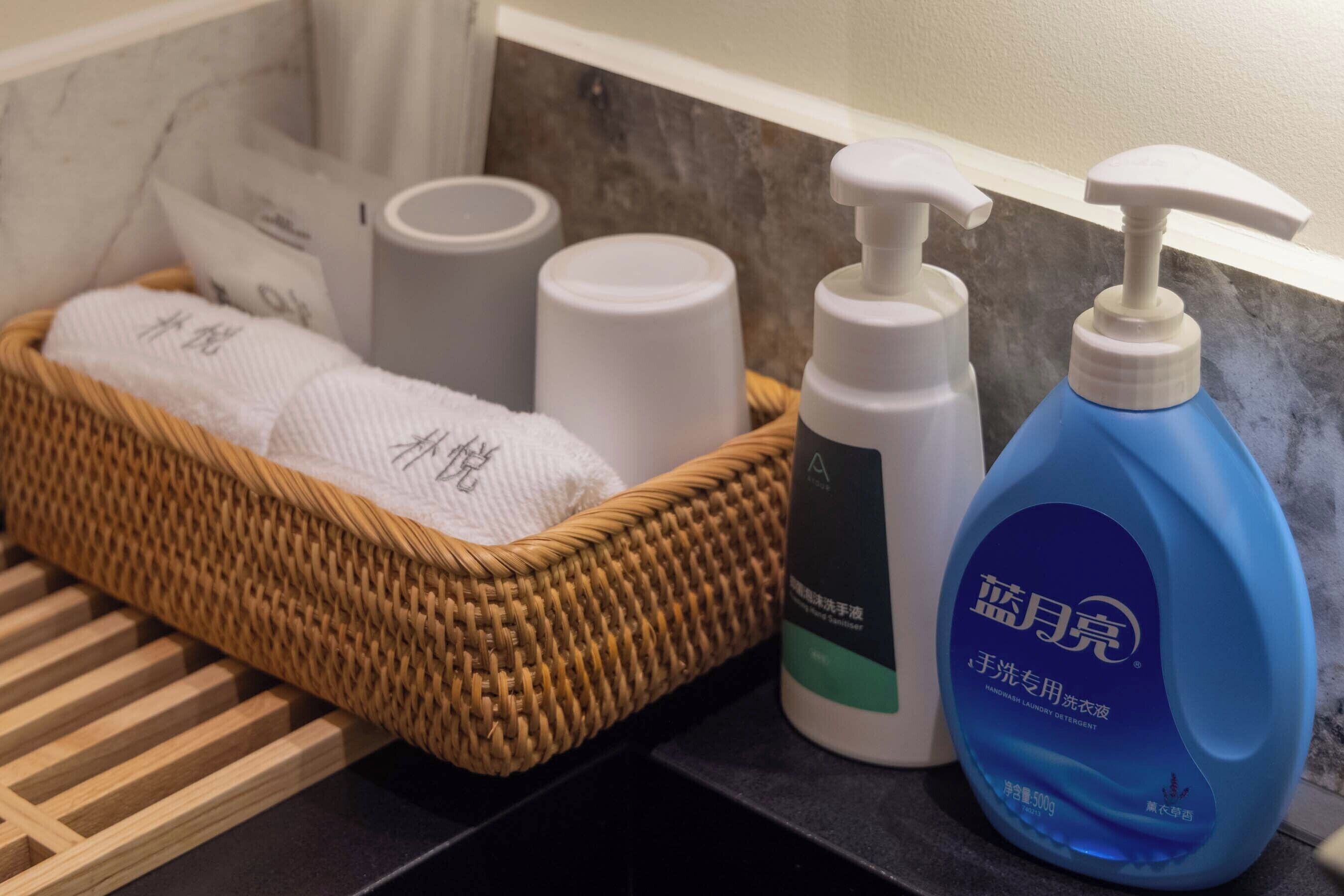 Un baño con una cesta de mimbre que contiene toallas, una botella blanca y una botella azul con dosificador.