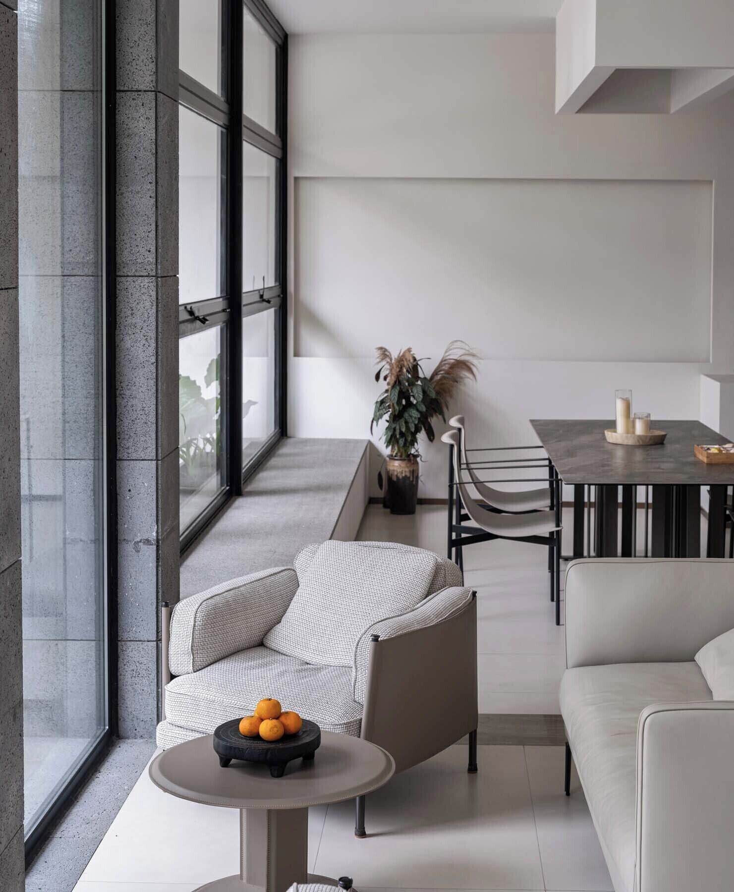A modern living room with a sofa, a round table with fruit, a dining table with chairs, and a potted plant.