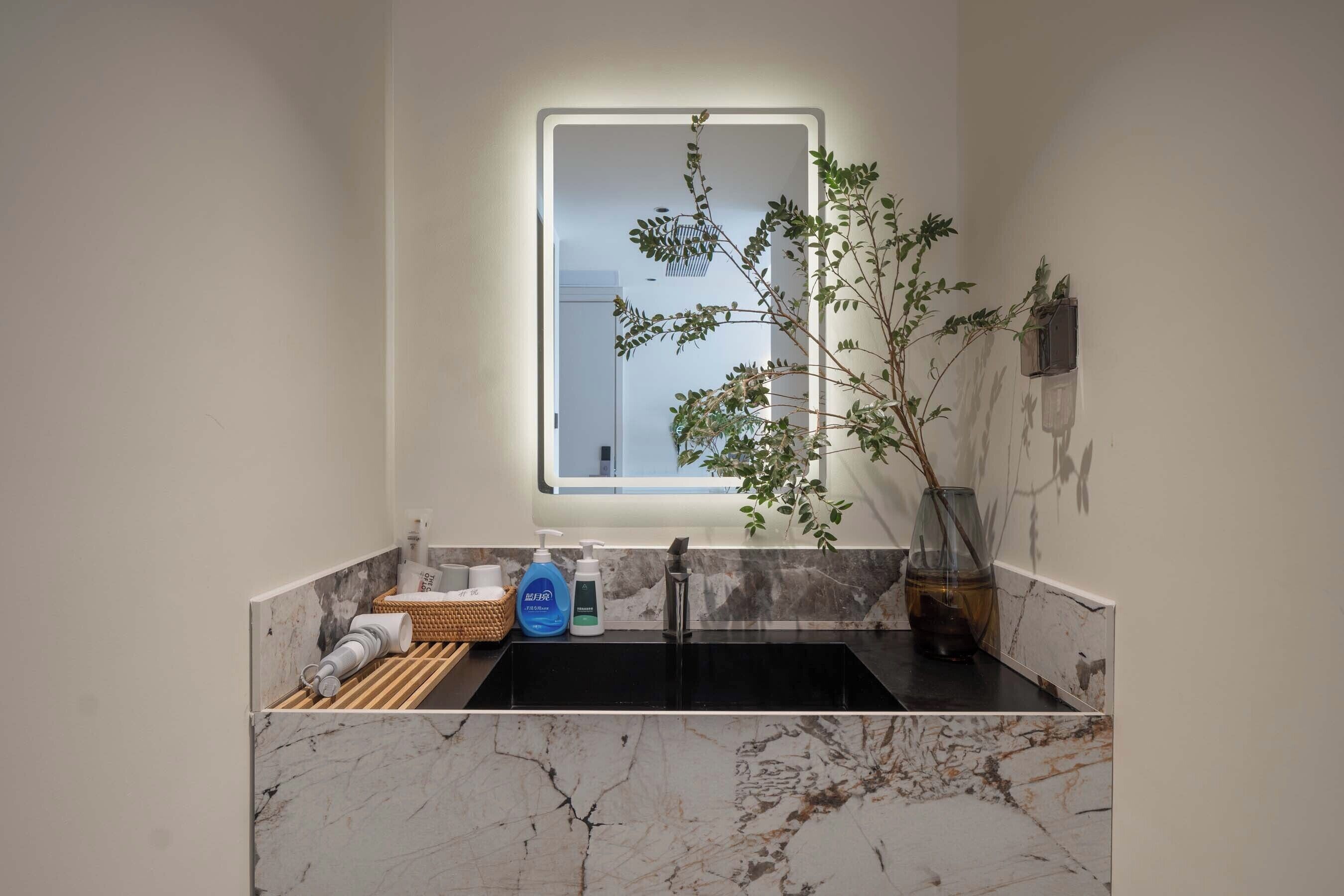 A bathroom with a marble sink, a window with a plant, and toiletries on the counter.