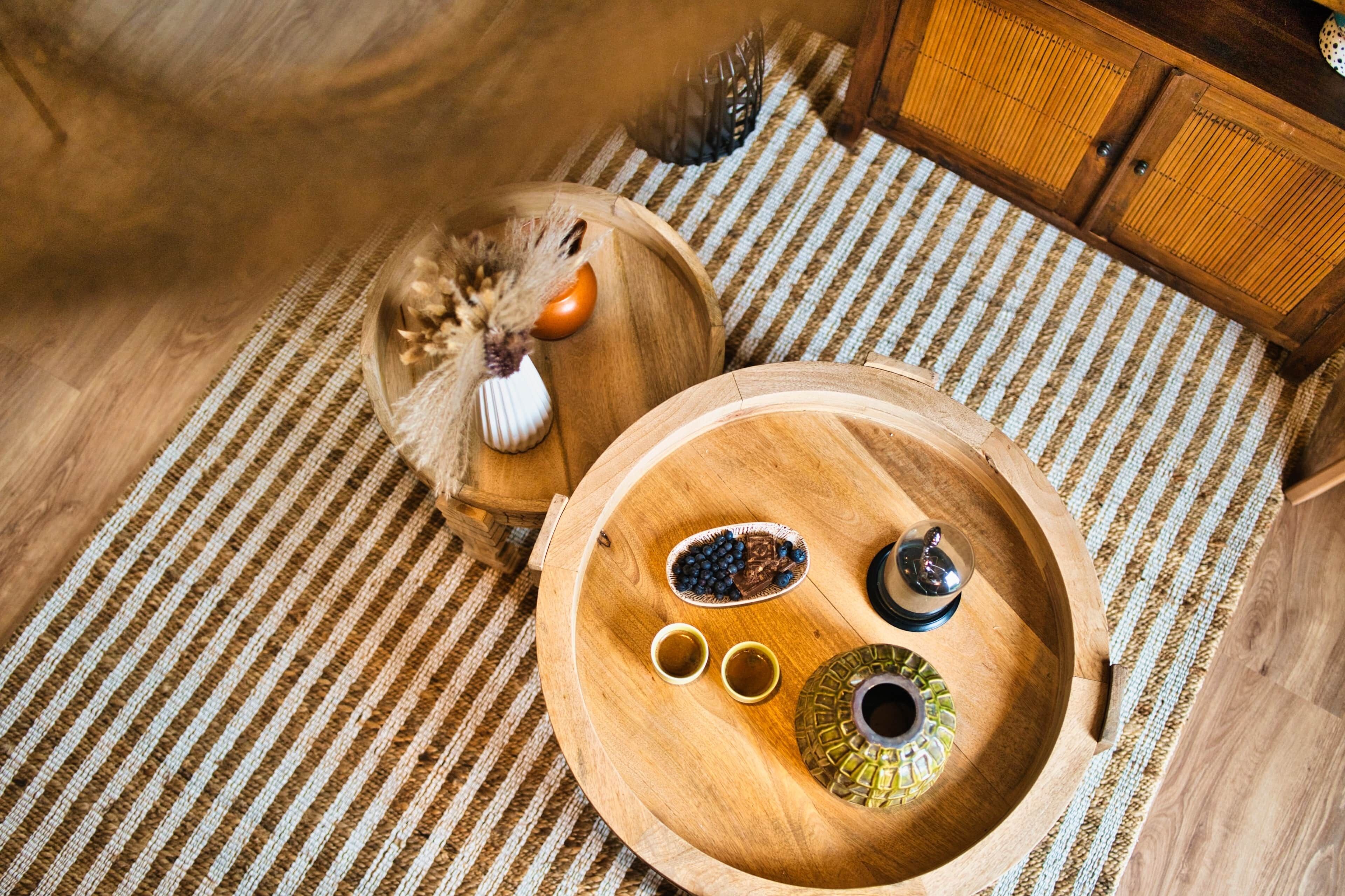 A wooden tray with a bowl of blueberries, two cups, and a decorative item on a woven mat.