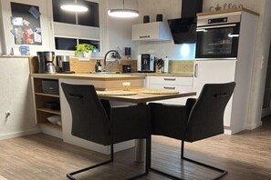 Eine moderne Küche mit Essbereich, darunter eine Kaffeemaschine, ein Spülbecken und ein Kühlschrank.
