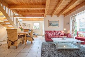 Ein Holzinnenraum mit Treppe, einem roten Sofa, einem Glastisch und einem Essbereich mit Korbstühlen.