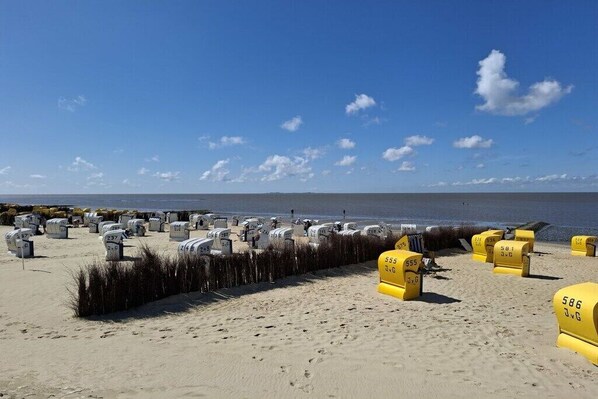Ein Strand mit zahlreichen Grabsteinen und gelben Markierungen, ein klarer Himmel und das Meer im Hintergrund.