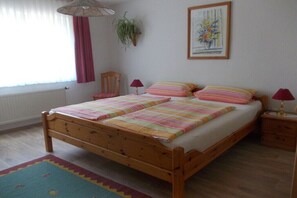 Un letto di legno con copripiumino a righe, una lampada da comodino, un quadro appeso al muro e una finestra con tende.