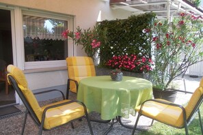 Un patio con tavolo e sedie, una finestra con tenda e piante in vaso fiorite.