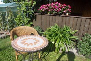 Eine Terrasse mit einem Korbstuhl und einem Tisch aus Mosaiksteinen, umgeben von Pflanzen und einem Holzzaun.