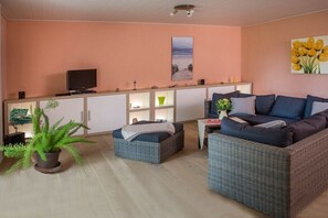 Ein Wohnzimmer mit Sofa, Hocker, Fernseher und einer Pflanze.