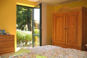 Ein Schlafzimmer mit einem Bett, einem Holzschrank, einem Schminktisch und einer Glastür, die zu einem Garten führt.